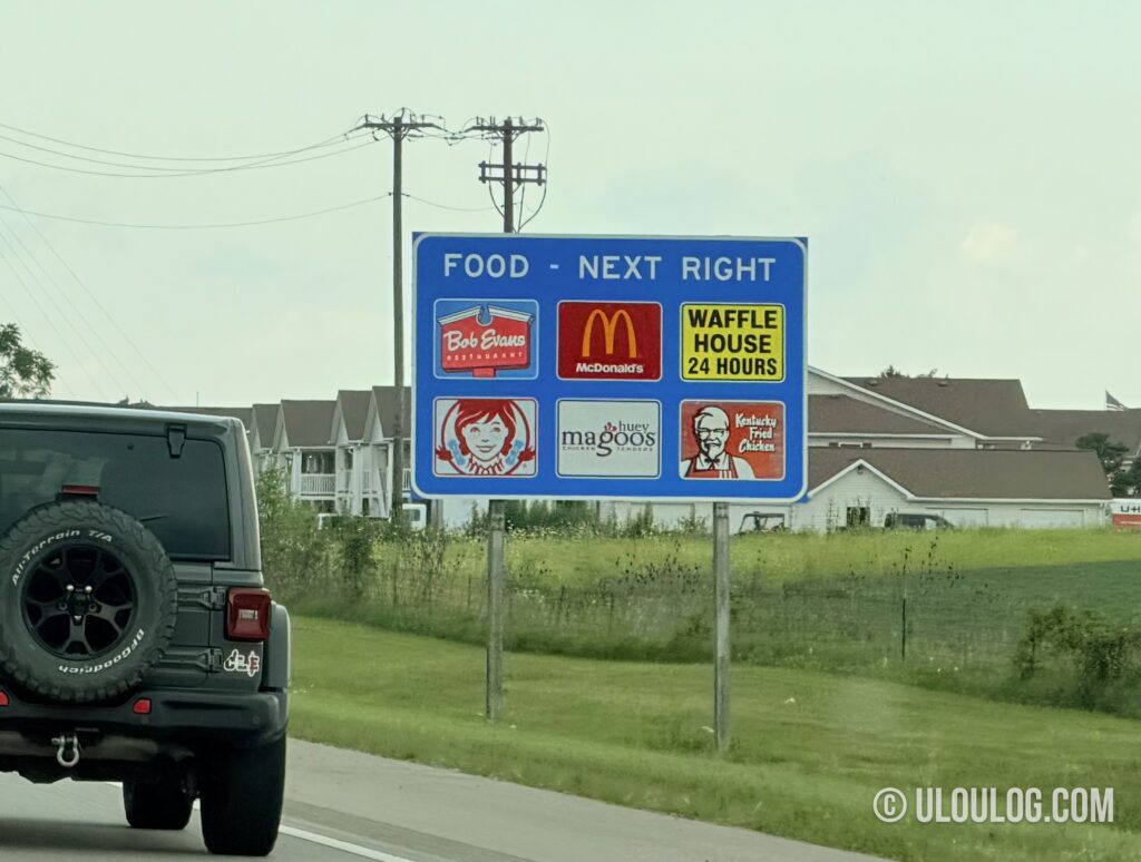 アメリカの高速道路のExit手前に立つFOODの青看板。飲食チェーン6軒のロゴが並ぶ
